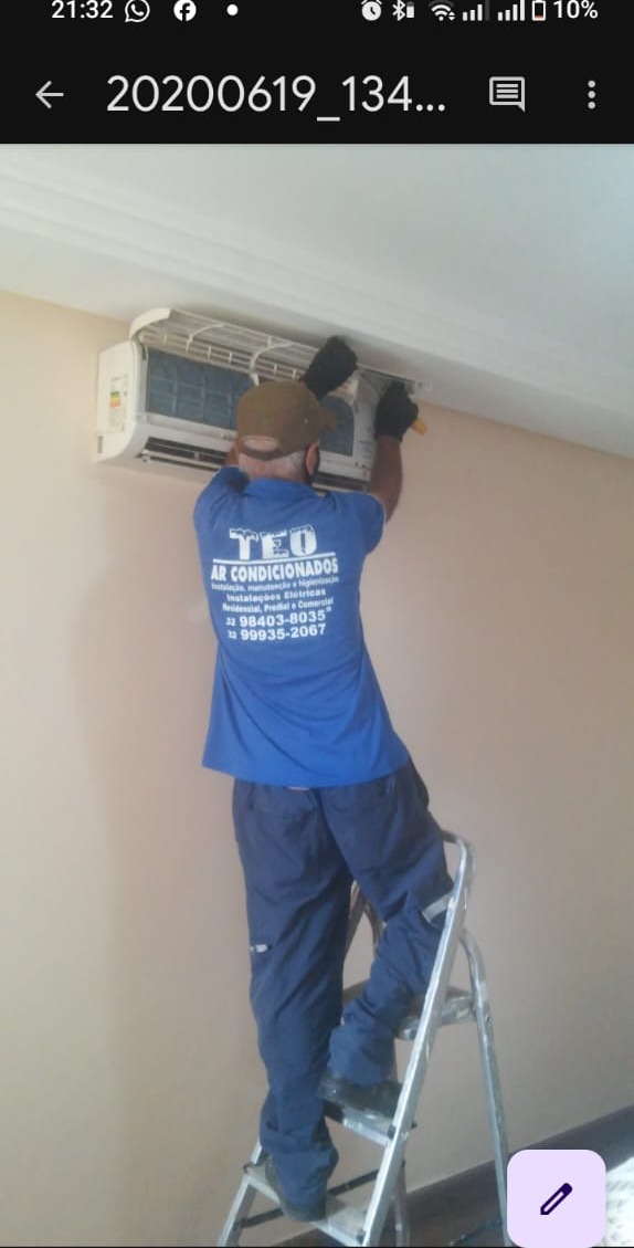 técnico de camiseta azul da TEO Ar-Condicionado em cima de uma escada consertando um split na parede