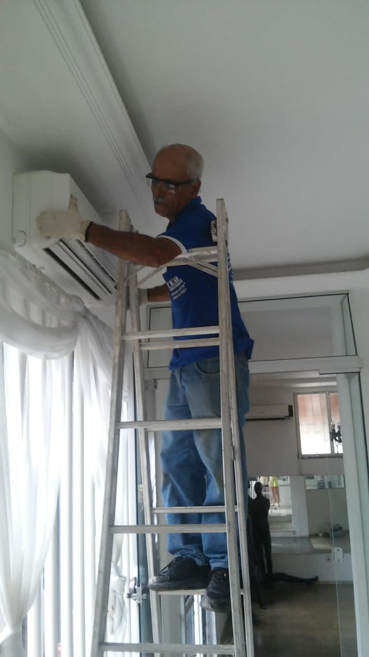 técnico em uniforme azul da TEO sobre escada instalando ar-condicionado split em residência